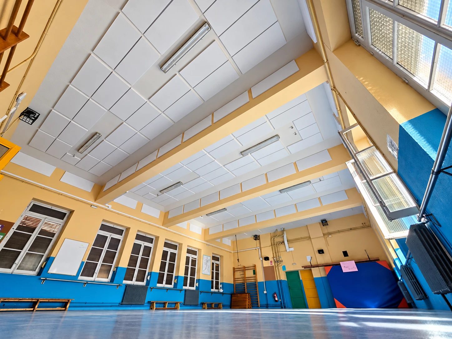 Gimnasio escolar con el techo entre vigas y los frisos revestidos de placas blancas de espuma t&eacute;cnica