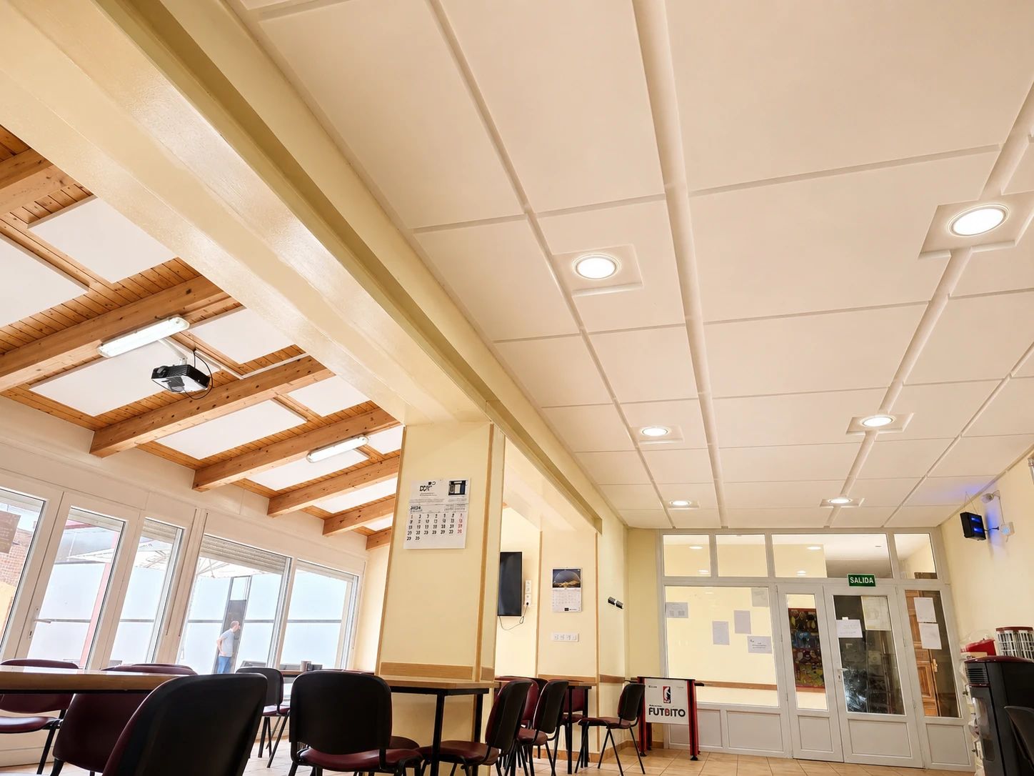 Sala de usos m&uacute;ltiples con techo de placas blancas de espuma t&eacute;cnica y zona de vigas de madera