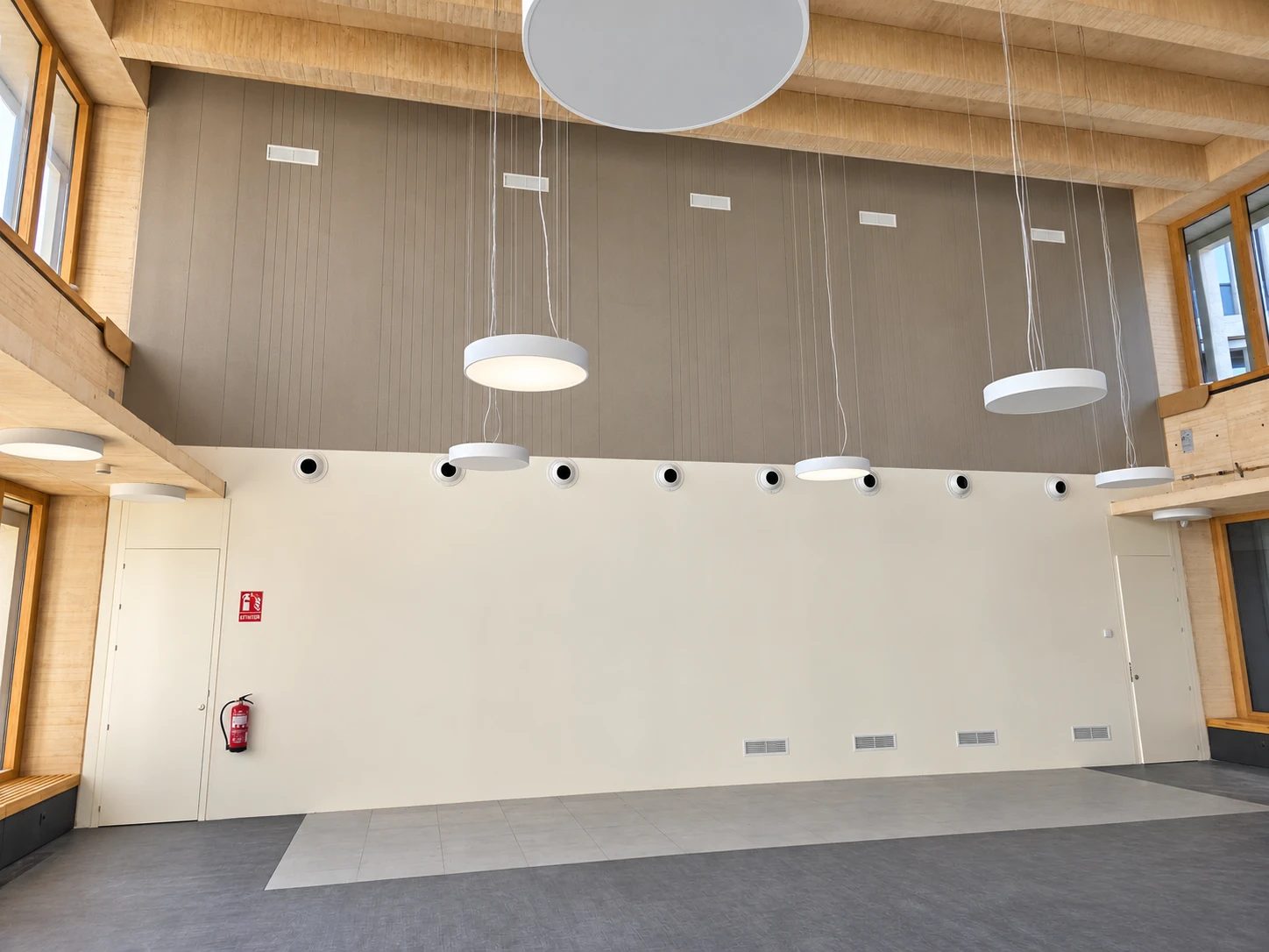 Resultado final: sala de doble altura con la franja alta del muro revestida de PET gris con ranurado vertical